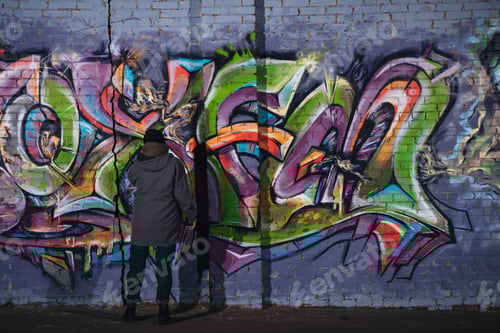 Visualização: vista traseira do artista de rua pintando grafites coloridos na parede à noite