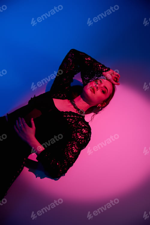 Preview: Stylish young woman poses elegantly in studio with vibrant pink and blue lighting