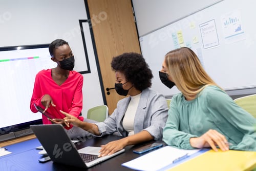 Preview: Diverse group of business colleagues wearing masks in discussion in meeting room looking at tablet