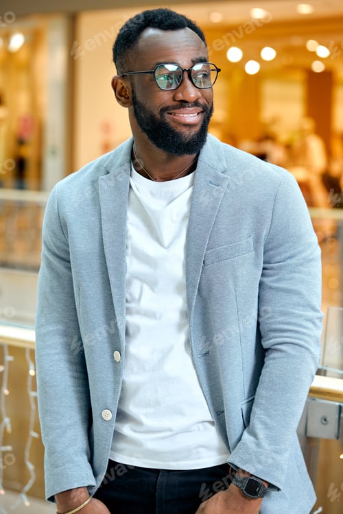 Preview: happy young african american man standing with hands on pockets in shopping mall