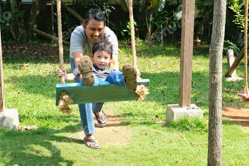 Preview: A joyful father helping his young son on a swing in a sunny, lush garden.