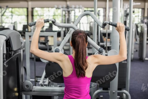 Preview: Fit woman using weight machine in gym