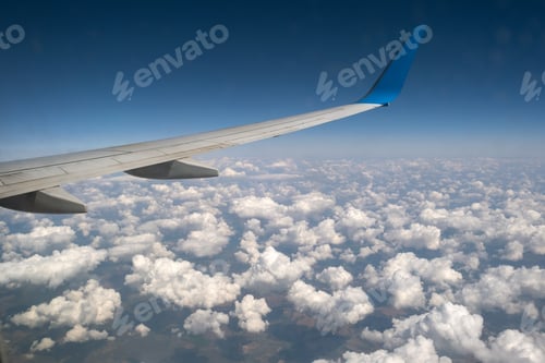Preview: View of jet airplane wing from inside flying over white puffy clouds in blue sky.