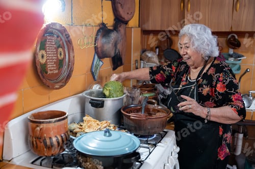 Preview: A senior mexican woman is smiling while preparing chayote to go with battered poblano chiles