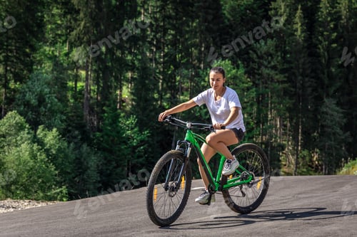 Preview: A young woman rides a bicycle in a mountainous area in the forest.