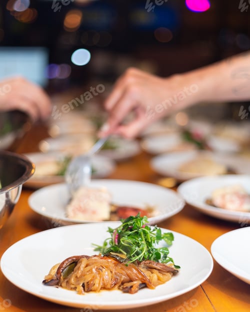 Preview: Selective focus shot of a hand preparing delicious food with greens on white plates