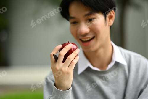 Preview: Happy asian man student eating apple during break in campus. People, education and lifestyle