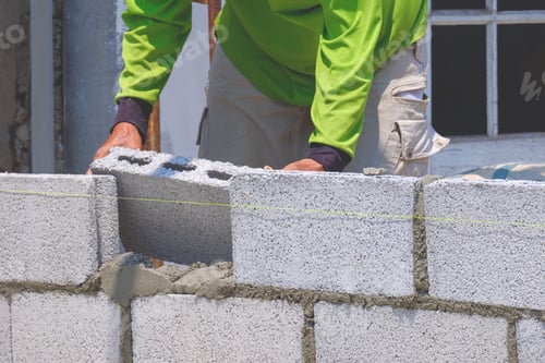 Preview: Cropped image of Bricklayer making concrete block wall inside of house construction site
