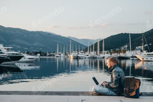 Preview: Freelancer working on laptop on the shore near the yacht boat at rest