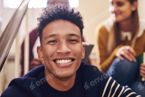 Preview: Cropped portrait of a handsome young male student sitting on a campus staircase with his friends