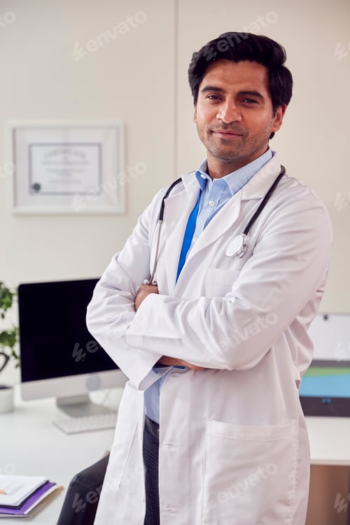 Preview: Portrait Of Male Doctor Or GP with Stethoscope Wearing White Coat Standing In Office