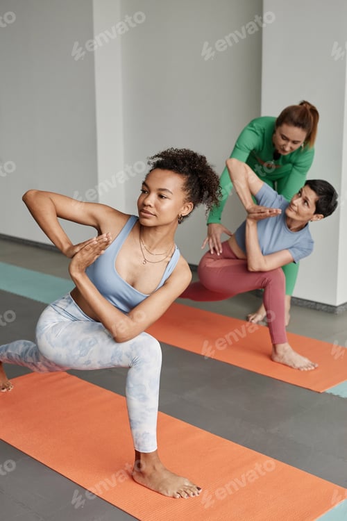 Preview: Young Women Stretching in Yoga Studio with Instructor Assisting