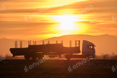 Preview: Semi-truck with cargo trailer driving on highway hauling cut down trees in evening. Timber delivery
