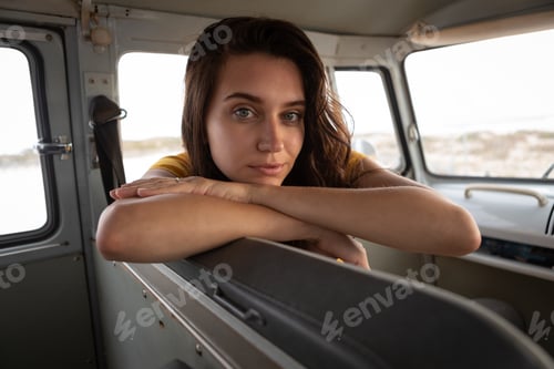 Preview: Beautiful woman sitting in camper van and looking at the camera against beach in background