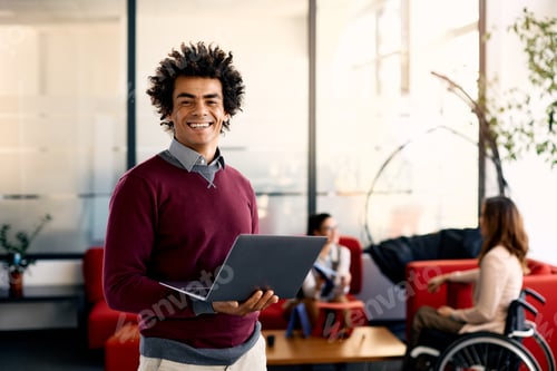 Preview: Happy black businessman using laptop in the office and looking at camera.