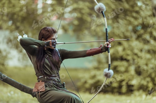 Preview: Woman with arrows and bow sits on a fallen tree and takes aim at a target