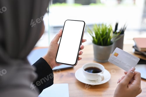 Preview: Over shoulder view of Muslim woman holding credit card and using mobile phone.