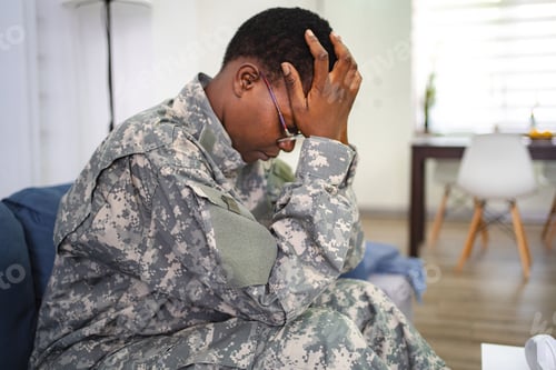 Preview: Depressed soldier suffering from post-traumatic stress disorder sitting on sofa at home