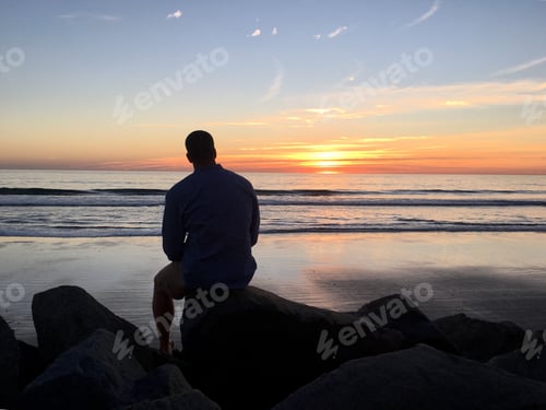Preview: Man’s silhouette watching sun set into ocean