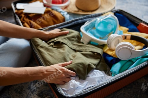 Preview: Male hands putting cloth into travel bag with summer clothing