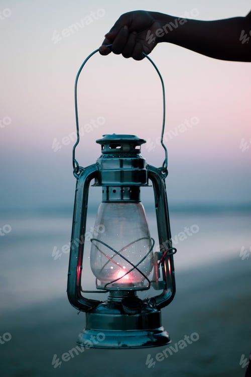 Preview: Vertical shot of a hand holding a lantern on a beach in the evening