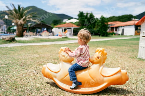 Preview: Little child sits on a swing in the playground on the beach. Side view