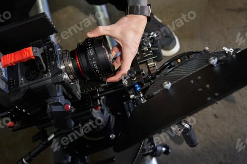 Preview: caucasian operator's hand unscrews the lens from a professional video camera. film camera with a