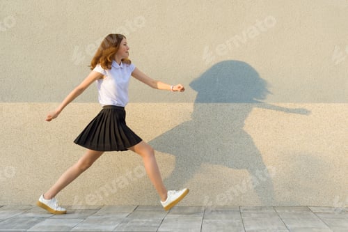 Preview: Young girl in the profile, walks along the gray wall, hurry, is late, takes big steps. Outdoor, copy