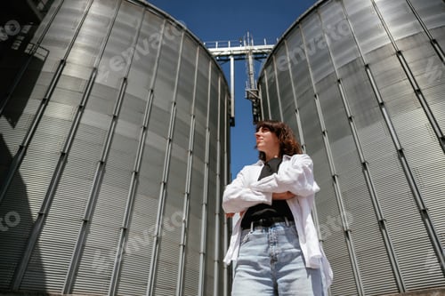 Preview: Confident worker standing in front of industrial silos under clear blue sky