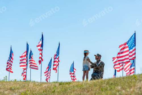 Preview: selective focus of father in military uniform looking at daughter near american flags