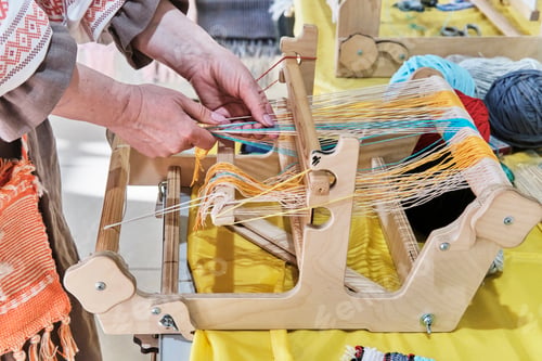 Preview: Female hands threading colorful warp threads on table loom.