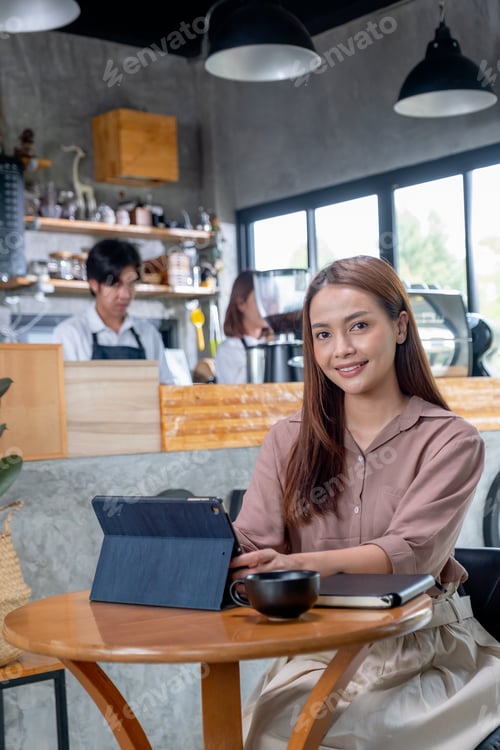 Preview: Beautiful Asian woman work with tablet in coffee shop, she also look at camera