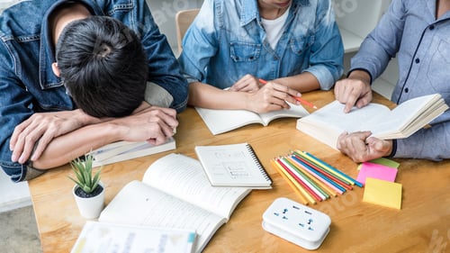 Preview: High school or college student group sitting at desk in library studying and reading