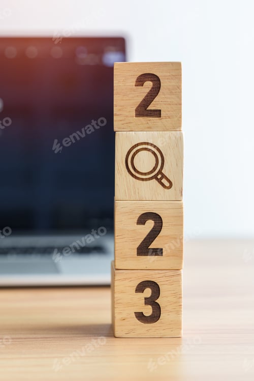 Preview: 2023 block with magnifying glass icon against laptop background.