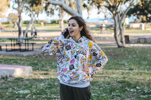Preview: Cute young teenager girl talking with friends by phone. Pretty teen outside at the trees