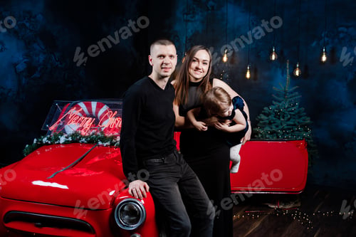 Preview: mom, dad and little daughter in love in Christmas are hugging near a red retro car with New Year's g