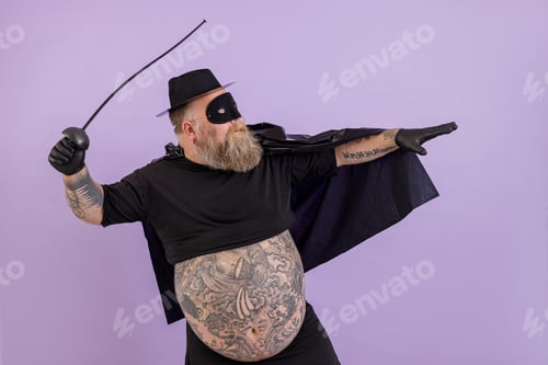 Preview: Fat man in Zorro costume with bare abdomen stands in bellicose pose on purple background