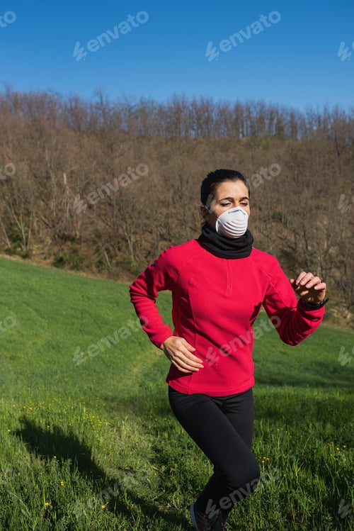 Preview: Vertical shot of a young Caucasian female running in a park wearing a protective medical mask