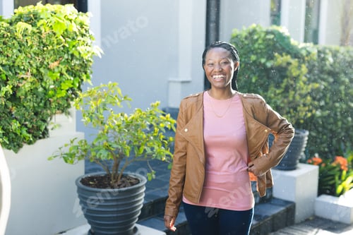 Preview: Portrait of happy african american woman wearing leather jacket standing outside house, copy space