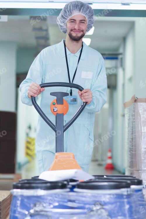 Preview: Smiling worker in a lab coat operating a manual forklift