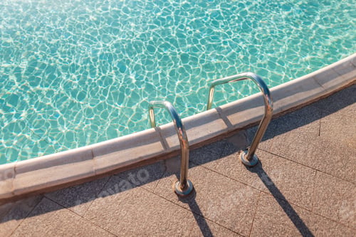 Preview: Beautiful swimming pool with azure blue water and metal descent at sunset, top view.