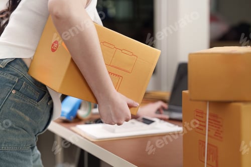Preview: E-commerce. Woman carrying package while managing online business in home office.