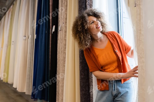 Preview: cheerful curly woman looking at different curtains in textile shop
