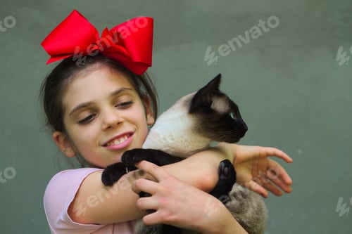 Preview: Closeup shot of a young Caucasian female with red bow on head holding her cat