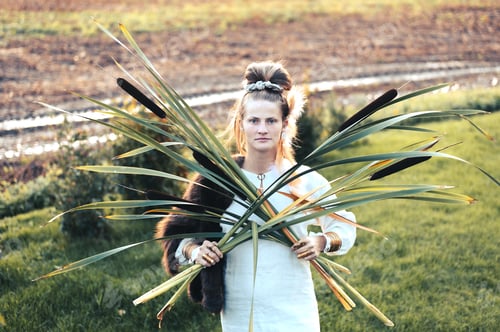 Preview: Strong young woman with a bulrush grass reed on rural field background at sunset