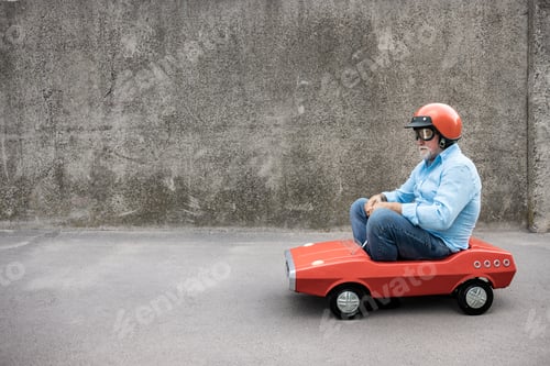 Preview: Funny businessman driving retro pedal car outdoor