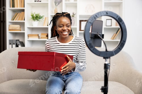 Preview: Cheerful Woman Unboxing Red Package During Video Call at Home