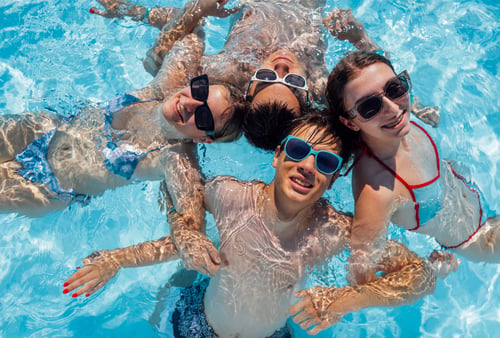 Preview: Smiling teenagers in swimsuits and sunglasses swim in the pool.
