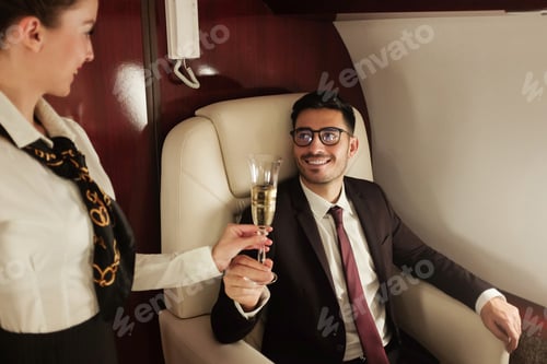 Preview: Businessman travelling in his private jet, meeting stewardess who brings him glass of champagne