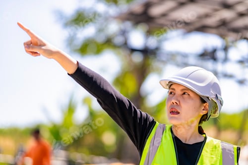 Preview: Engineer in safety vest and helmet pointing towards a solar powered carport
